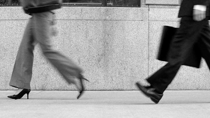 Black and white detail of two people walking past a stone wall